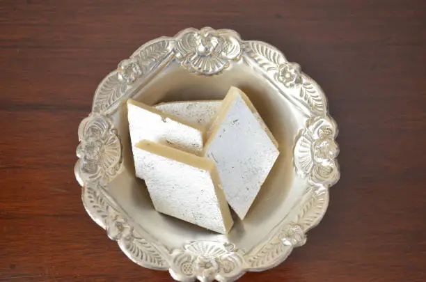 Kaju katli, also known as kaju barfi, is an Indian dessert similar to a barfi. Made from sugar, cashew, dryfruits, ghee, and saffron and cut into bite-sized diamond -shaped pieces. Silver foil on it.