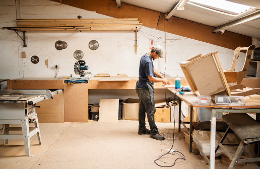 Worker standing alone at a bench in a furniture workshop and assembling a wooden chair