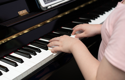 Side view of girl playing piano at home. Cute child learning to play musical instrument.