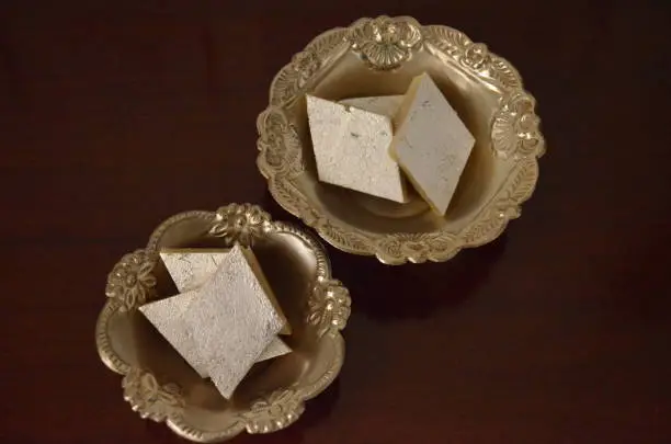 Kaju katli, also known as kaju barfi, is an Indian dessert similar to a barfi. Made from sugar, cashew, dryfruits, ghee, and saffron and cut into bite-sized diamond -shaped pieces. Silver foil on it.