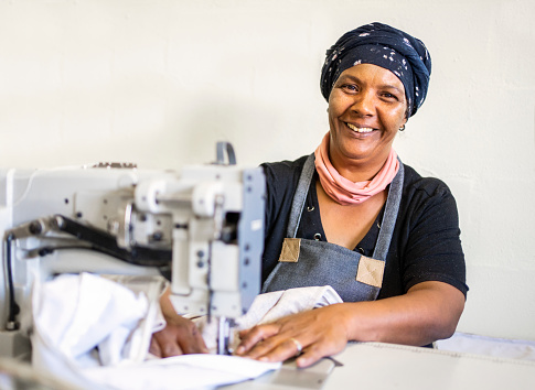 Portrait of a seamstress smiling while sewing a long piece of material using a sewing machine in an upholstery workshop