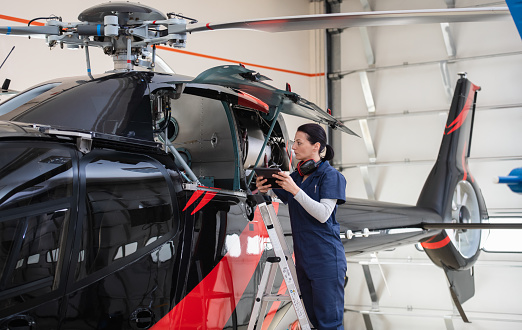 Female aero engineer with digital tablet, working and checking helicopter. Safety and aviation concept.