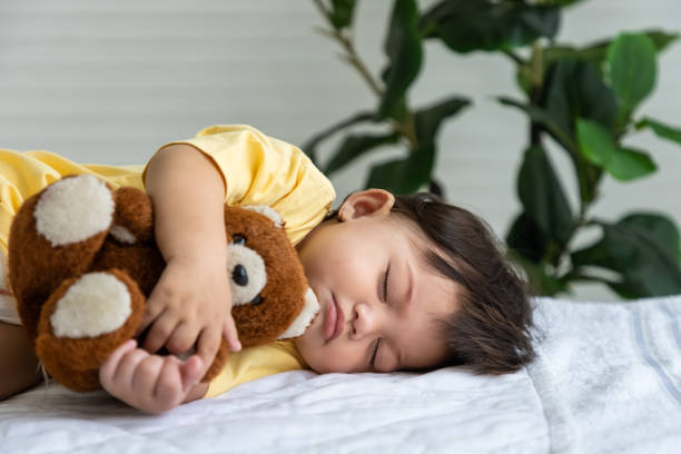 menina asiática deitada dormindo na cama em casa, abraçando boneca de urso de pelúcia. criança recém-nascida relaxando na cama. berçário para crianças pequenas. - newborn little girls baby lying down - fotografias e filmes do acervo