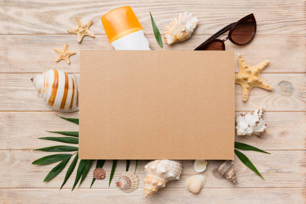 Summer time concept with blank greeting card and blank craft paper on colored background. Seashells from ocean shore in the shape of frame separated with space for text top view