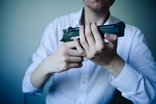 A young man holds a pistol in his hands. He is in a living room.