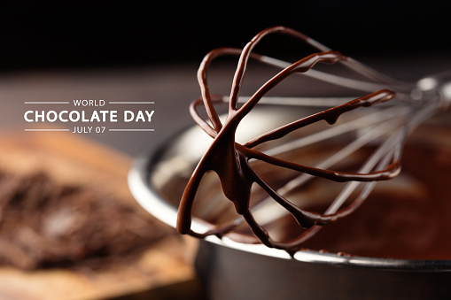 World Chocolate Day, 7 july. Melted homemade chocolate cream in bowl with whisk on wooden background, selective focus. Holiday greeting card or banner concept.