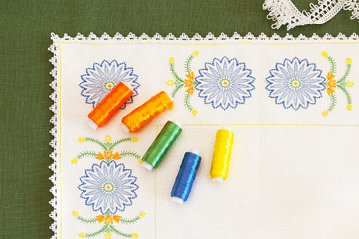 Napkin with embroidery in the form of cornflowers and spools of thread located on it, with which embroidery and lace are made. Embroidery as a kind of creativity and needlework.
