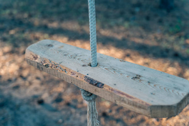 istock Empty single-rope swing on a rope. Wooden swing and rope with a knot. Close-up. Selective focus. 1405215807