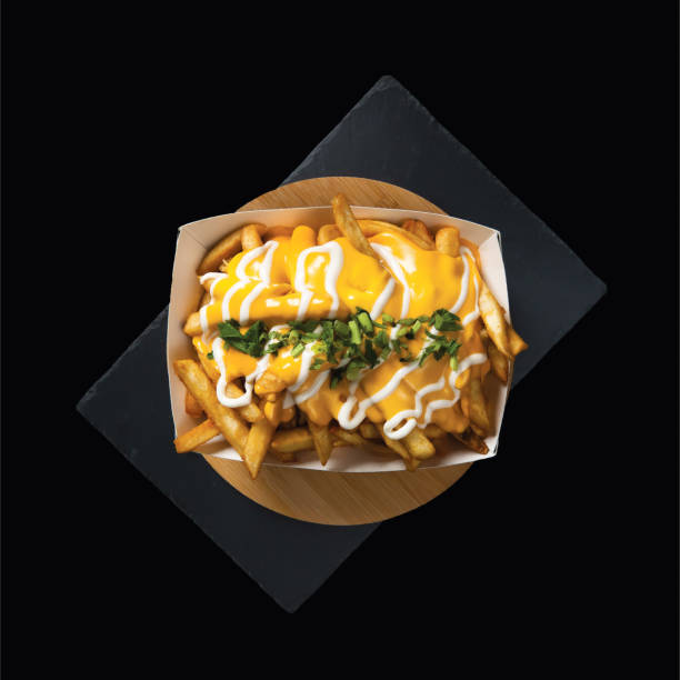 Loaded Cheese Fries served in a box isolated on wooden board top view on black background fast food stock photo