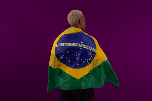 Black-skinned man holding the flag of Brazil and wearing the shirt of the Brazilian soccer team in studio photo
