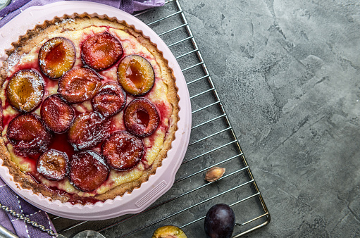 Home baked plum pie with fresh plums on a concrete background top view. Copyspace area.
