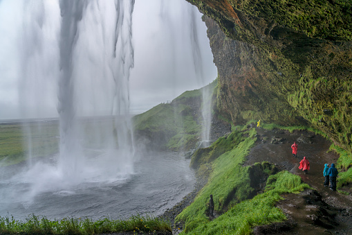 Some tourists walking under the Seljalandsfoss waterfall on rainy day in Iceland