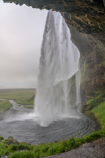 Some tourists walking under the Seljalandsfoss waterfall on rainy day in Iceland