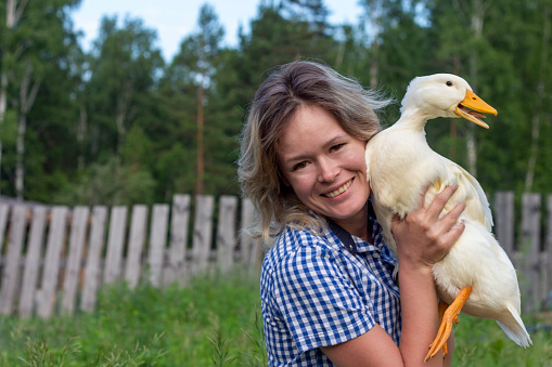 Portrait of pretty young woman embracing white duck in the farm on the grass