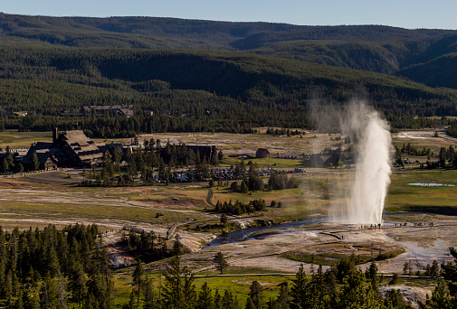 Beehive Geyser springs to life in front of Old Faithful Inn on golden hour at Yellowstone National Park