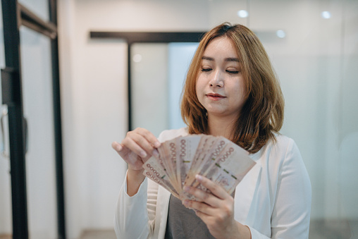 Young pretty woman is looking at cash banknotes, Thai Currency. Financial, profit, credit, cost, purchase, rich concept.