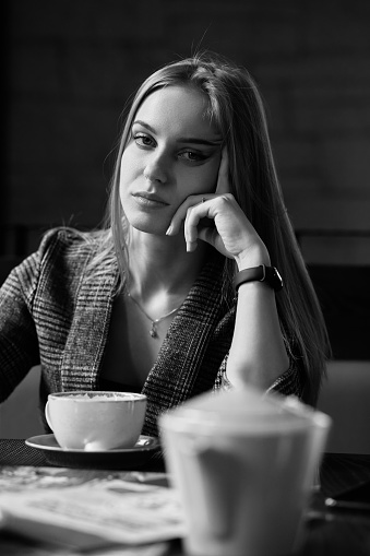 serious young blond woman with cup of tea in cafe, looking at camera, monochrome