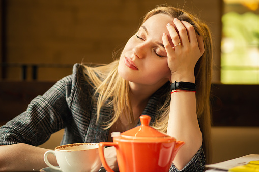 young blond girl with a teapot at cafe with closed eyes, longs misses, dreams, hand on head