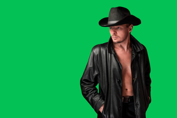 Cowboy in a leather jacket looks away. Unshaven serious man in a hat isolated on a green background. Looking away. Culture of Western America