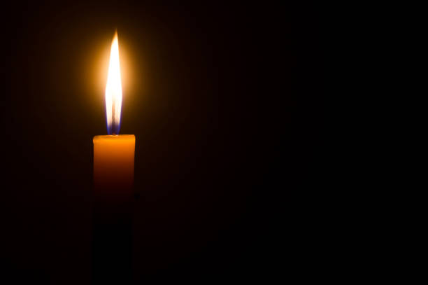 istock A single burning candle flame or light glowing on a yellow candle isolated on black or dark background on table in church for Christmas, funeral or memorial service 1405241175