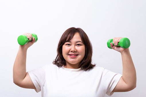 Young Asian chubby woman hold dumbbell for exercise and weight training. Fighting while diet during weight loss program with positive emotion. Portrait shot on white background.