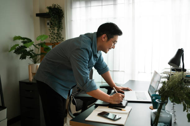 istock Happy man writing on digital tablet while Virtual meeting with partner on laptop computer at home. Virtual work concepts 1405242450