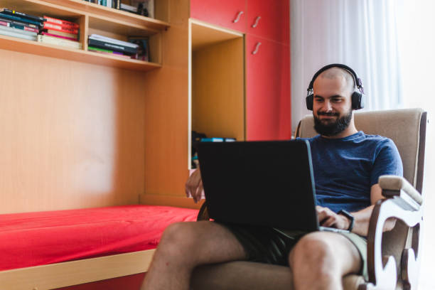 istock Happy bald young man using his laptop computer at home while wearing headphones 1405253184