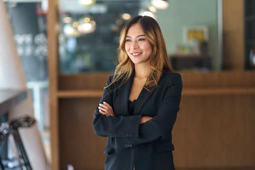 Hermosa y sonriente mujer de negocios asiática de pie con los brazos cruzados en la oficina mirando por la ventana. photo