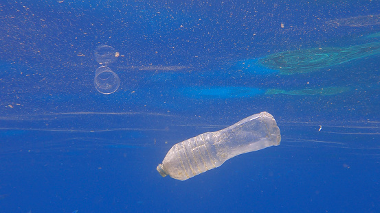 Plastic pollution, plastic bottle and cup in blue water. Discarded plastic bottle slowly drifting under surface of blue water in sunlight. Plastic garbage environmental pollution problem in Red Sea, Egypt