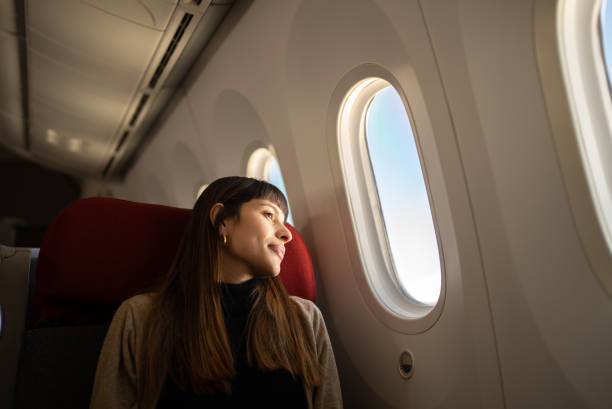 jeune femme voyageant en avion en regardant par la fenêtre - airport passengers photos et images de collection