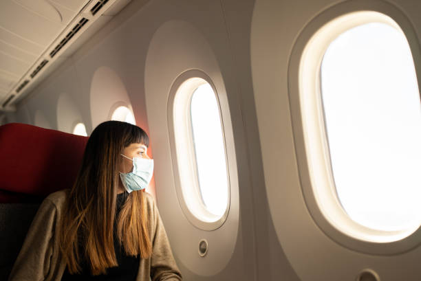 istock Young woman traveling by plane with mask while looking out the window 1405263247