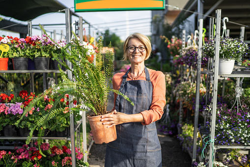 Portrait of a female florists standing alone in garden center outdoors, she is holding a potted plant.