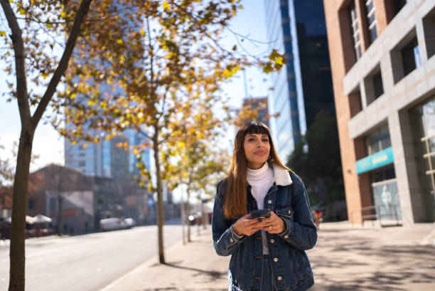 istock Young woman walking while using mobile phone in the city 1405265630