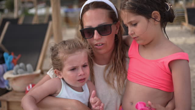 Blind Caucasian mother consoling her daughters on the beach