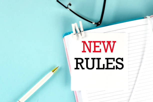 NEW RULES text on a sticky on notebook with pen and glasses , blue background stock photo