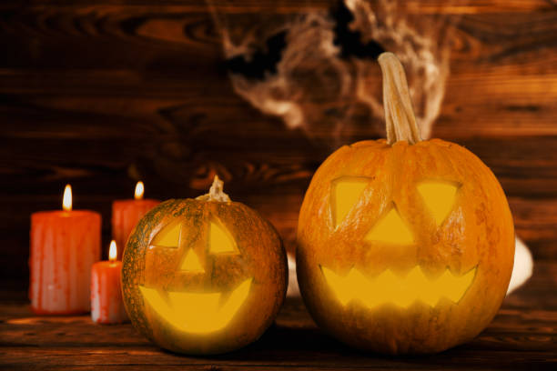 istock Halloween pumpkin on brown wood texture with candles. Composition on a dark background. Scary composition with glowing eyes and mouth. Holiday concept. copy space 1405270030