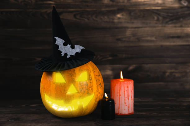 istock Halloween pumpkin on brown wood texture with candles. Composition on a dark background. Scary composition with glowing eyes and mouth. Holiday concept. copy space 1405270100