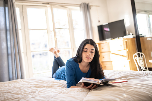 Mid adult woman reading a book on the bed at home