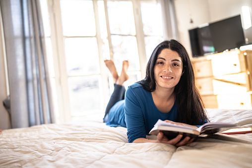 Portrait of a mid adult woman reading a book on the bed at home