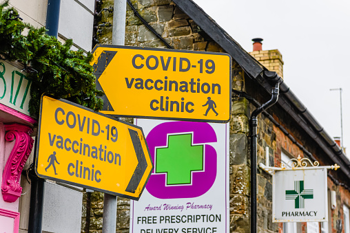 Strangford, Northern Ireland - 26 January, 2022: Yellow pedestrian direction signs for a COVID-19 walk-in vaccination clinic at a local village pharmacy where they offer COVID-19 vaccines without an appointment.