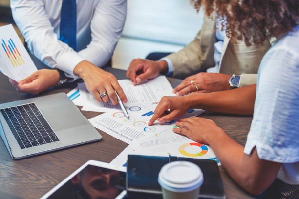 Close up of people pointing to a graph with data. Close up of people pointing to a graph with data. There is also a digital tablet and a laptop on the table. economy stock pictures, royalty-free photos & images