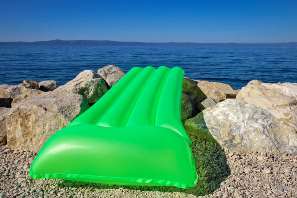 A green inflatable mattress lies on the stone seashore