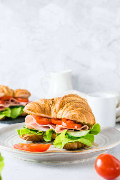 kanapka z rogalikiem z szynką, ogórkami, pomidorem i sałatą na talerzu na stole. widok pionowy. - bun salad ham rolled up zdjęcia i obrazy z banku zdjęć