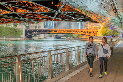 Chicago, IL - September 28, 2021: People walk along the famous Riverwalk park, passing under one of the iconic draw bridges downtown, in the Loop.