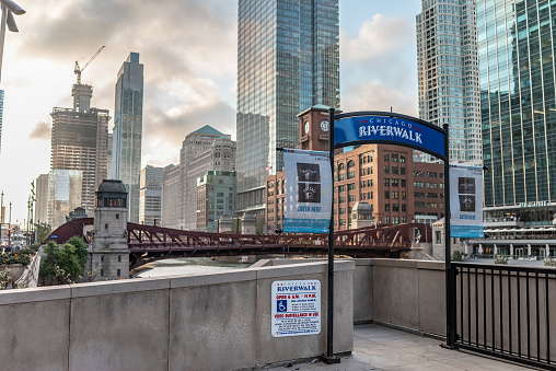 Chicago, IL - September 28, 2021: Sign at the entrance to the famous Riverwalk park along the Chicago River, with the city skyline beyond, at sunset.