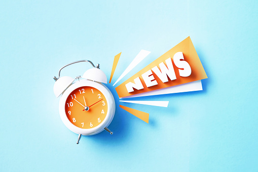 News reads next to white alarm clock on blue background. Horizontal composition with copy space. News concept.