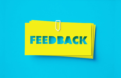 Feedback written cut out yellow adhesive notes sitting on turquoise background. Horizontal composition with copy space.