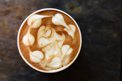 Cappuccino coffee with hearts pattern in a perfect circle and dark stone background