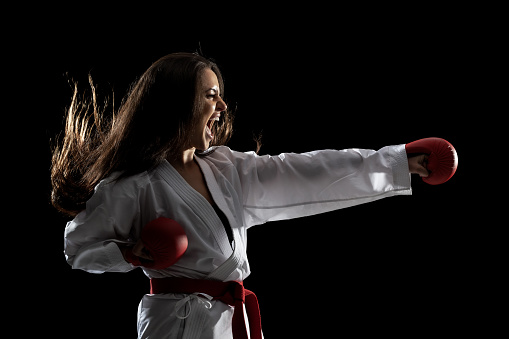 girl exercising karate punch and screaming against black background