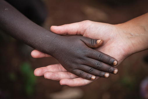 Multiracial human hands in one of African villages, Ethiopia, East Africa. Young caucasian female volunteer holding hand of African child